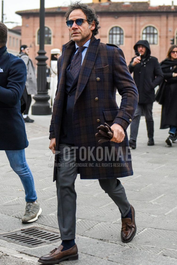 Men's coordinate and outfit with plain sunglasses, navy-brown check chester coat, plain navy tailored jacket, plain light blue shirt, plain gray slacks, plain gray socks, and brown tasseled loafer leather shoes.