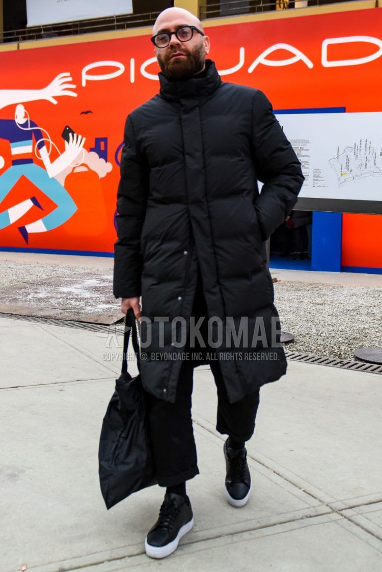 Men's coordinate and outfit with solid black glasses, solid black down jacket, solid black cotton pants, solid black socks, black low-cut sneakers, and solid black briefcase/handbag.