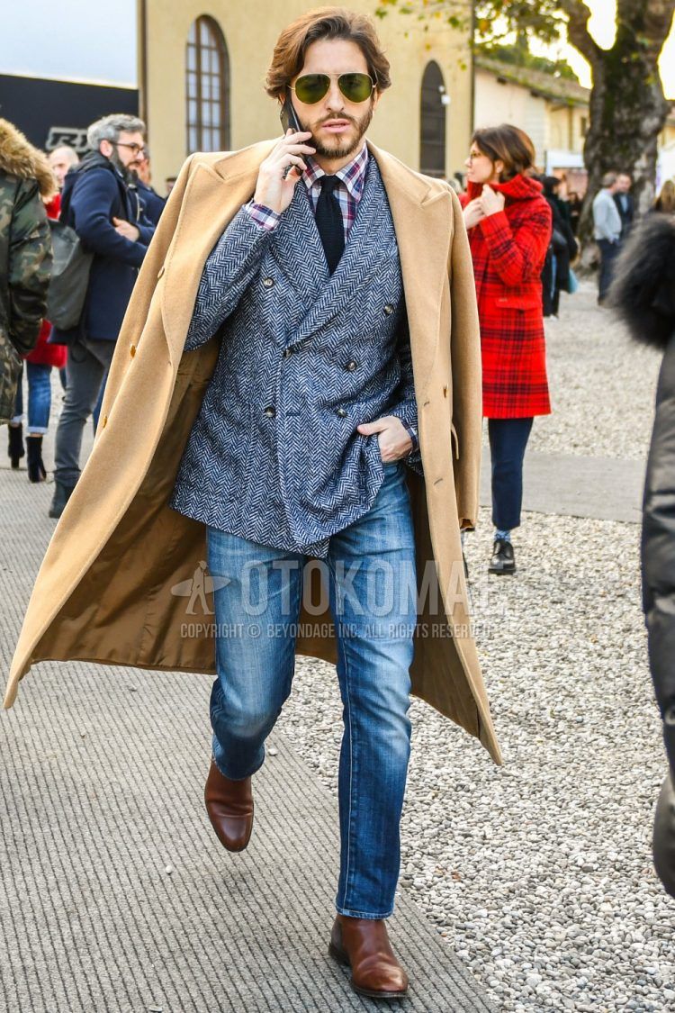Men's coordinate and outfit with plain sunglasses, plain beige chester coat, gray herringbone tailored jacket, red checked shirt, solid blue denim/jeans, brown side gore boots, solid navy knit tie.