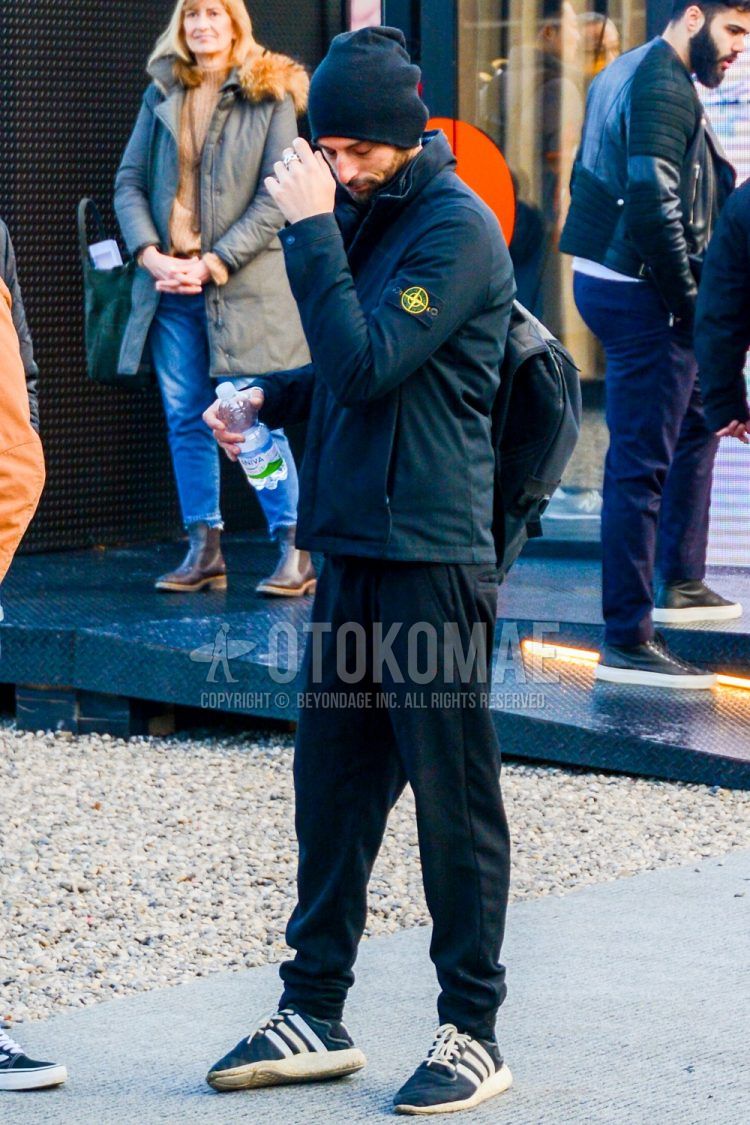 Men's coordinate and outfit with plain black knit cap, plain black down jacket from Stone Island, plain black sweatpants, and black low-cut sneakers from Adidas.