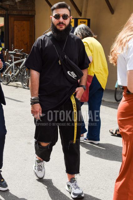 Men's coordinate and outfit with brown tortoiseshell sunglasses, plain black t-shirt, off-white yellow taped belt, plain black damaged jeans, plain pink socks, Nike white and gray low-cut sneakers, Nike black deca logo body bag.