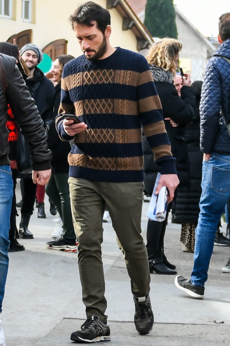 Men's coordinate and outfit with navy/beige striped sweater, olive green plain cotton pants, and premierta gray/black low-cut sneakers.