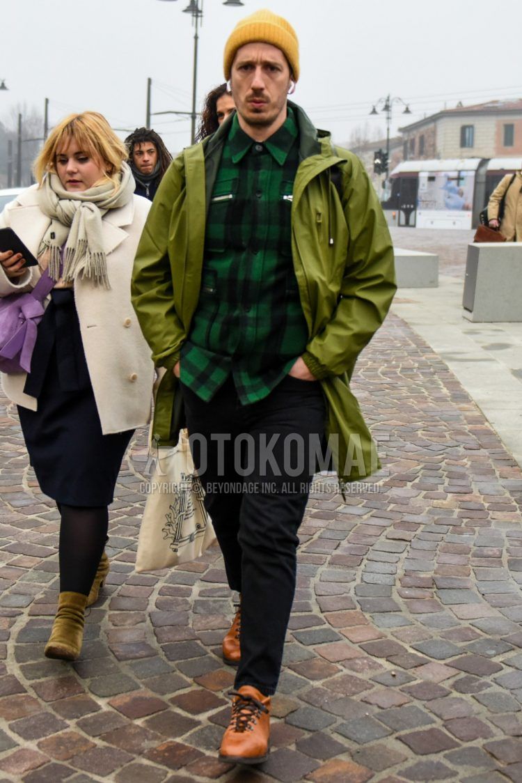 Men's coordinate and outfit with solid yellow knit cap, solid green hooded coat, green checked shirt, solid black denim/jeans, and brown boots.