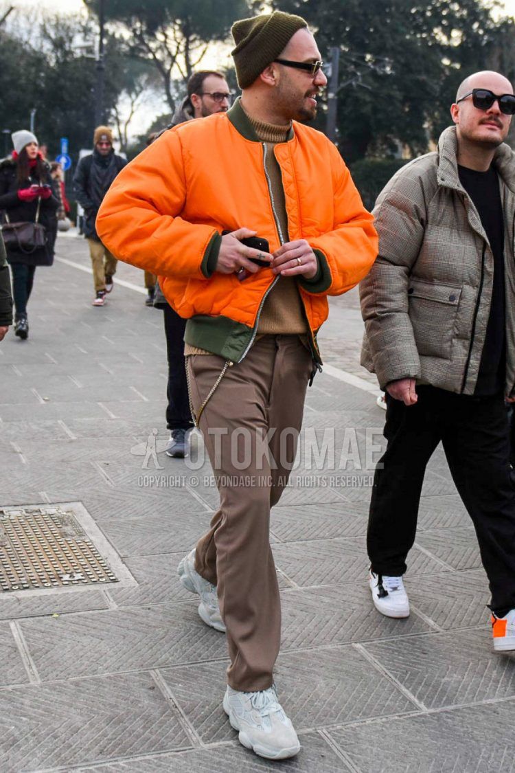 Men's coordinate and outfit with olive green solid color knit cap, orange solid color MA-1, brown solid color turtleneck knit, brown solid color bottoms, and white low-cut sneakers.