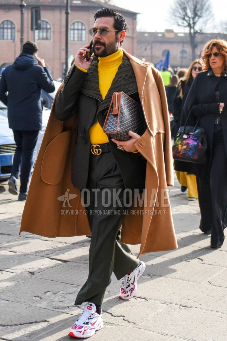 Solid color glasses, solid color beige chester coat, solid color gray cardigan, solid color yellow turtleneck knit, solid color black Gucci leather belt, solid color gray socks, white low cut Nike sneakers, gray Goyard bag clutch/second bag/drawstring, Men's coordinate/outfit with plain gray suit.