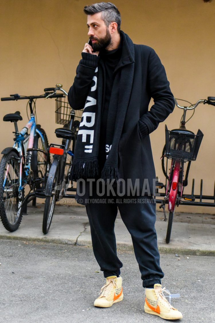 Men's coordinate and outfit with black graphic scarf/stall, solid black outerwear, solid black sweater, solid black sweatpants, and Nike orange high-cut sneakers.