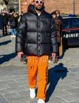 Men's coordinate and outfit with orange one-point knit cap, plain white sunglasses, plain black down jacket, orange graphic sweatpants, and white low-cut sneakers.