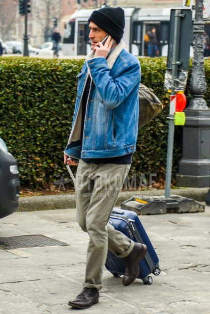 Men's coordinate and outfit with solid black knit cap, solid blue denim jacket, solid black trainers, solid beige chinos, brown straight tip leather shoes, and solid blue suitcase.