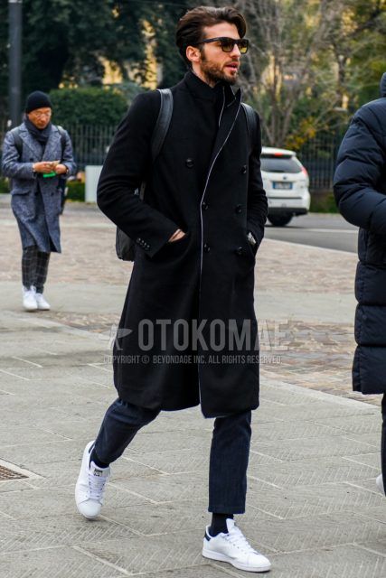 Men's coordinate and outfit with solid color sunglasses, solid color black chester coat, solid color navy denim/jeans, solid color black socks, and white low-cut Adidas sneakers.