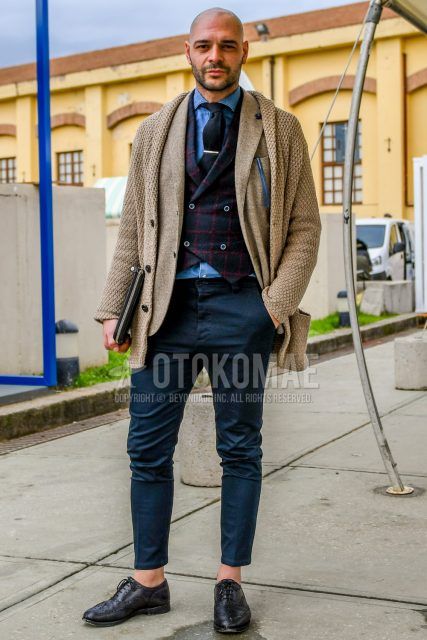 Men's coordinate/outfit with solid beige cardigan, solid beige tailored jacket, gray/red checked gilet, solid blue denim/chambray shirt, solid gray slacks, black wingtip leather shoes, and solid black tie.