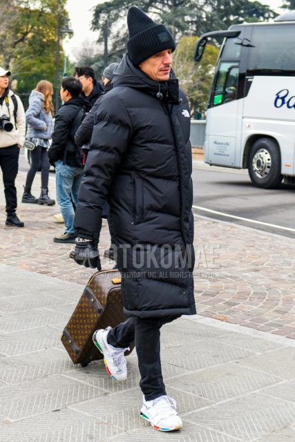 Men's coordinate and outfit with solid black knit cap, solid black down jacket from The North Face, dark gray solid denim/jeans, white low-cut sneakers, and solid brown bag from Louis Vuitton.