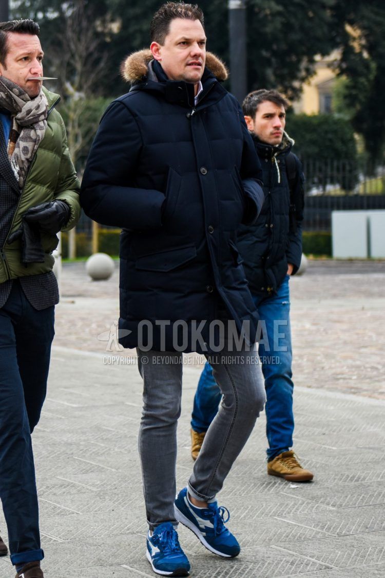 Men's coordinate and outfit with plain black down jacket, plain white shirt, plain gray denim/jeans, and Diadora blue low-cut sneakers.