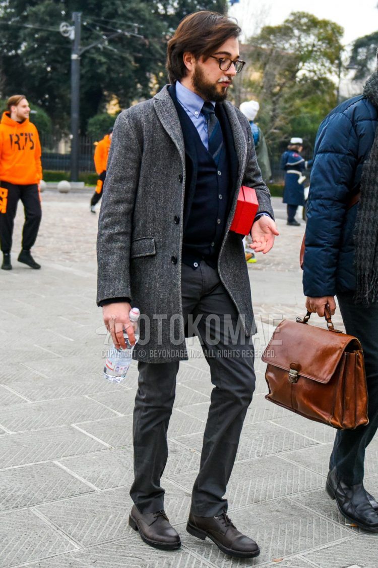 Men's coordinate and outfit with plain glasses, dark gray solid color chester coat, light blue solid color shirt, navy solid color cardigan, dark gray solid color slacks, brown straight tip leather shoes, and blue striped tie.