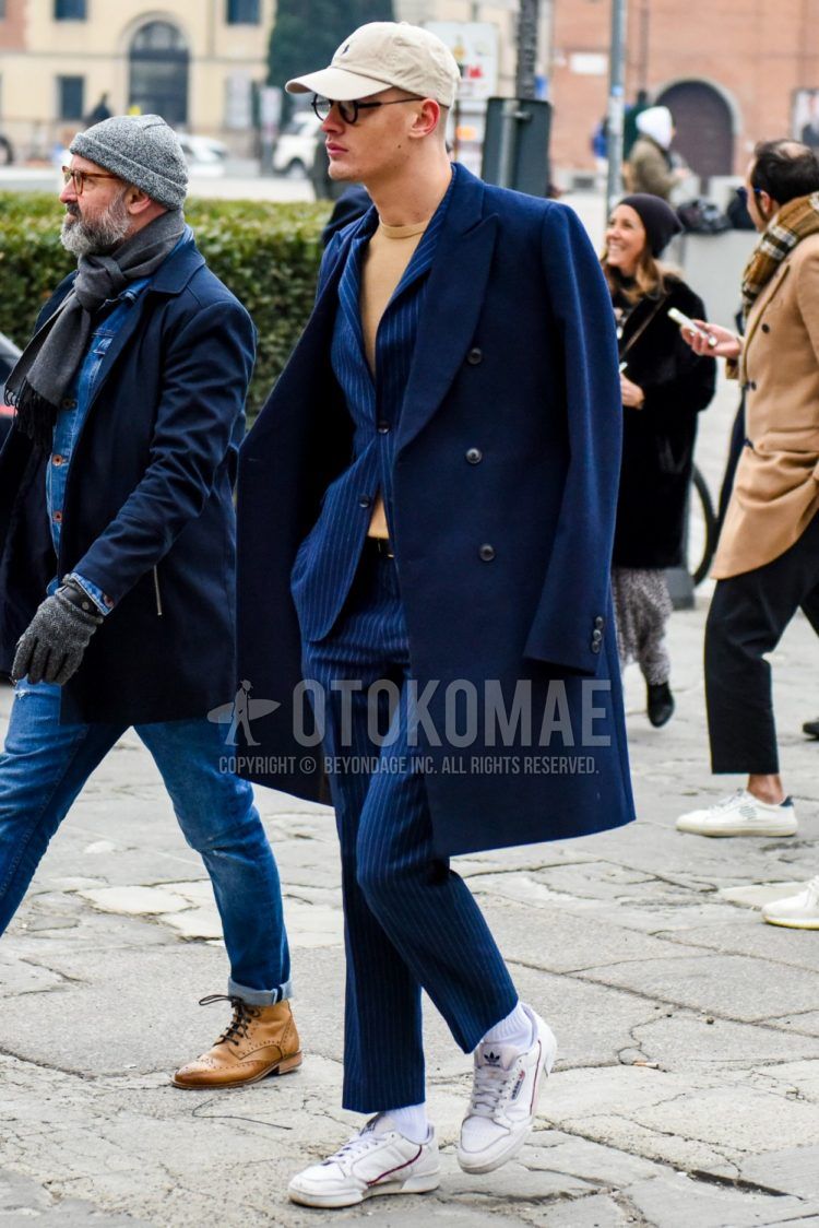 Men's coordinate and outfit with beige one-point baseball cap, plain black glasses, plain navy chester coat, plain beige sweater, plain leather belt, plain white socks, white low-cut Adidas sneakers, and navy striped suit.