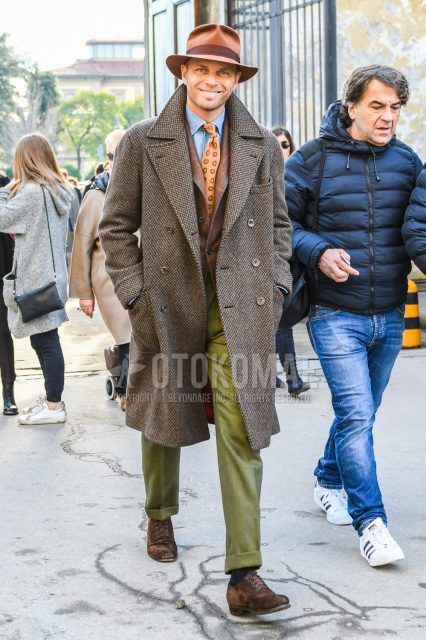 Solid brown hat, brown herringbone Ulster coat, solid brown tailored jacket, solid light blue denim/chambray shirt, solid olive green slacks, solid navy socks, suede brown plain toe leather shoes, orange small print tie Winter men's coordinate/outfit with orange small print tie.