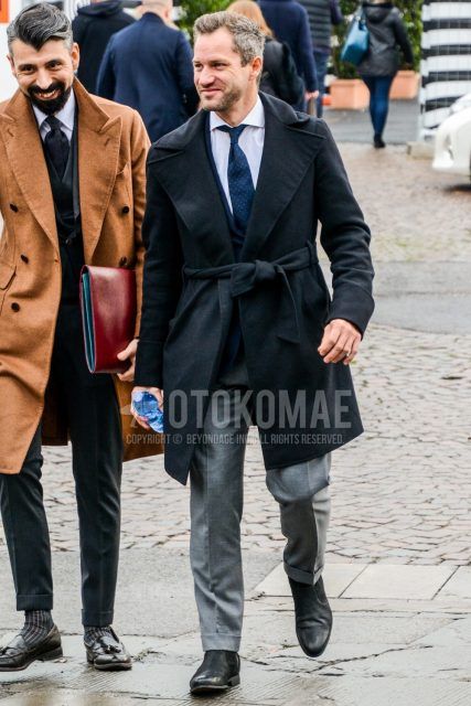 Men's coordinate and outfit with plain black belted coat, plain navy tailored jacket, plain white shirt, plain gray slacks, black side gore boots, and navy dot tie.