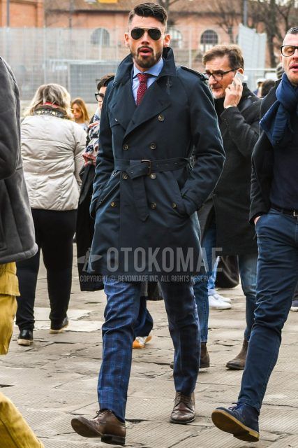 Men's winter coordinate and outfit with Ray-Ban teardrop gold solid sunglasses, solid black trench coat, solid light blue shirt, navy check slacks, brown brogue shoes leather shoes, and red tortoiseshell tie.