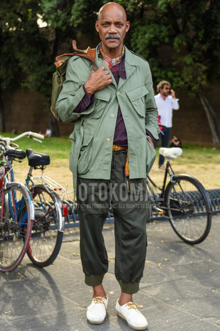 Men's coordinate and outfit with multi-colored stole bandana/neckerchief, solid green safari jacket, solid purple shirt, solid olive green jogger pants/ribbed pants, plain cargo pants, and white leather shoes.