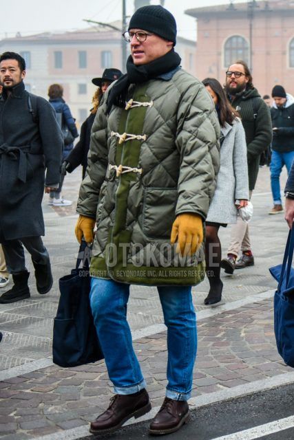 Men's outfit/clothing with plain navy knit cap, plain glasses, plain black scarf/stall, plain olive green quilted jacket, plain blue denim/jeans, brown boots, and plain navy briefcase/handbag.