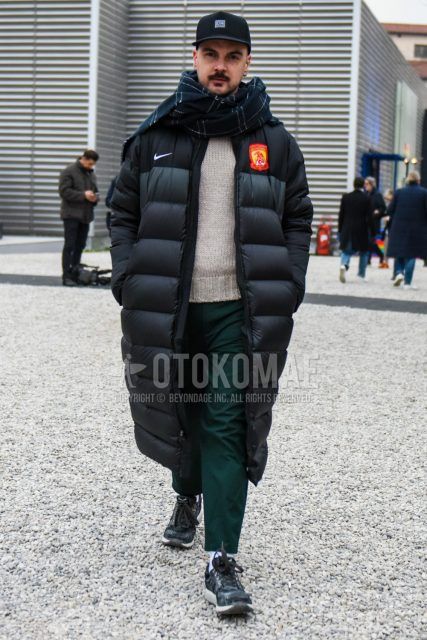 Men's coordinate and outfit with black one-point baseball cap, black checked scarf/stall, Nike Manchester United solid black down jacket, solid beige sweater, solid green chinos, solid white socks, and black low-cut sneakers.