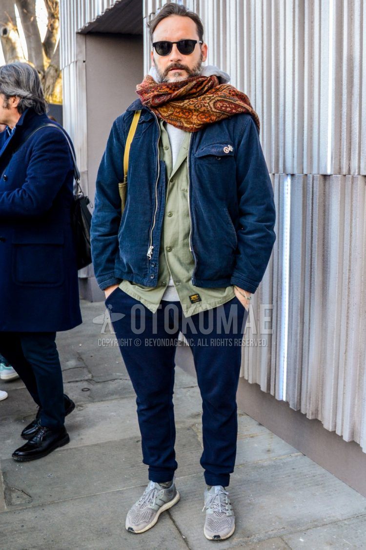 Men's coordinate and outfit with solid color sunglasses, multi-colored stole scarf/stall, solid color navy outerwear, solid color green shirt jacket, solid color gray hoodie, solid color navy jogger pants/ribbed pants, and ultra boost gray low cut sneakers.