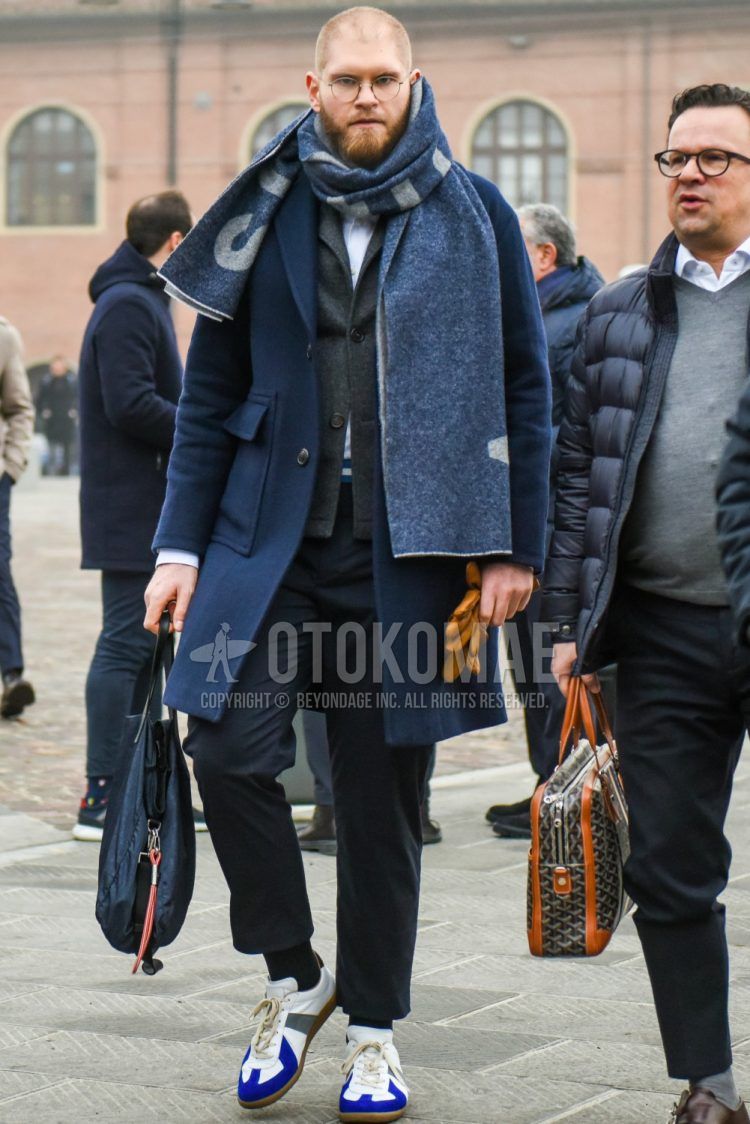 Men's outfit with navy scarf/stall, navy solid color chester coat, dark gray solid color tailored jacket, dark gray solid color ankle pants, black solid color socks, white low-cut sneakers, and navy solid color tote bag.