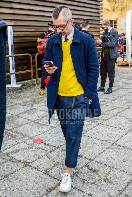 Men's coordinate and outfit with plain glasses, plain navy stainless steel coat, plain yellow sweater, plain white shirt, plain gray slacks, Diadora white low-cut sneakers, and gray-navy regimental tie.