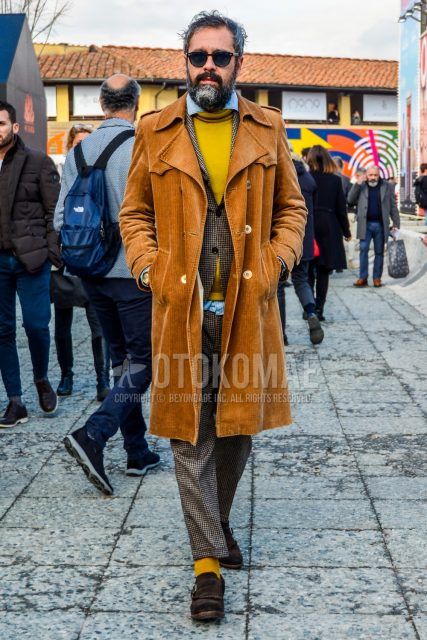 Men's coordinate and outfit with solid color sunglasses, solid color brown trench coat, solid color yellow sweater, solid color light blue denim/chambray shirt, brown monk shoes leather shoes, suede shoes leather shoes, brown checked suit.