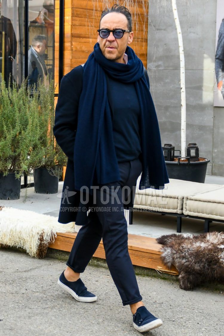 Men's coordinate and outfit with solid color sunglasses, solid color navy scarf/stall, solid color navy chester coat, solid color navy sweater, solid color dark gray bottoms, and navy slip-on sneakers.