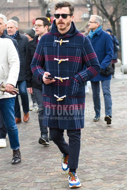 Men's coordinate and outfit with plain sunglasses, navy check duffle coat, plain gray slacks, plain black socks, and white, blue, and red low-cut sneakers.