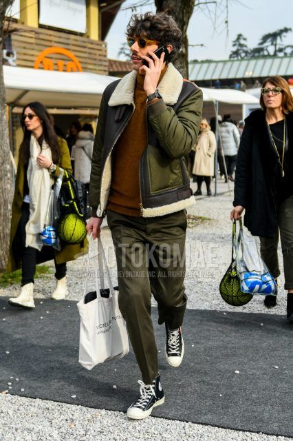 Men's coordinate with solid color sunglasses, solid color black and olive green leather jacket (not riders), solid color brown turtleneck knit, solid color olive green slacks, black high cut Converse All Star sneakers, beige decalogo tote bag. Outfit.