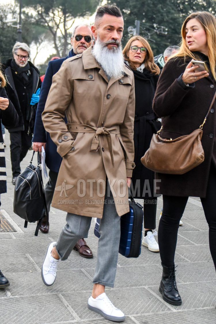 Men's coordinate and outfit with plain beige trench coat, plain gray slacks, white low-cut sneakers, and plain black briefcase/handbag.