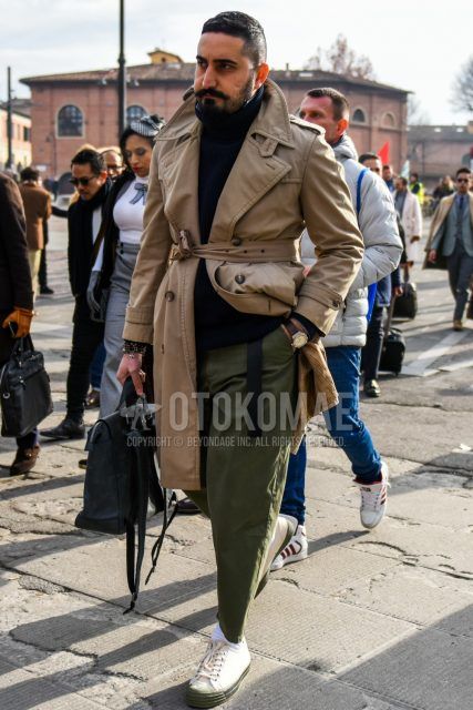Men's coordinate and outfit with plain beige trench coat, plain black turtleneck knit, plain olive green chinos, plain white socks, and white low-cut sneakers.