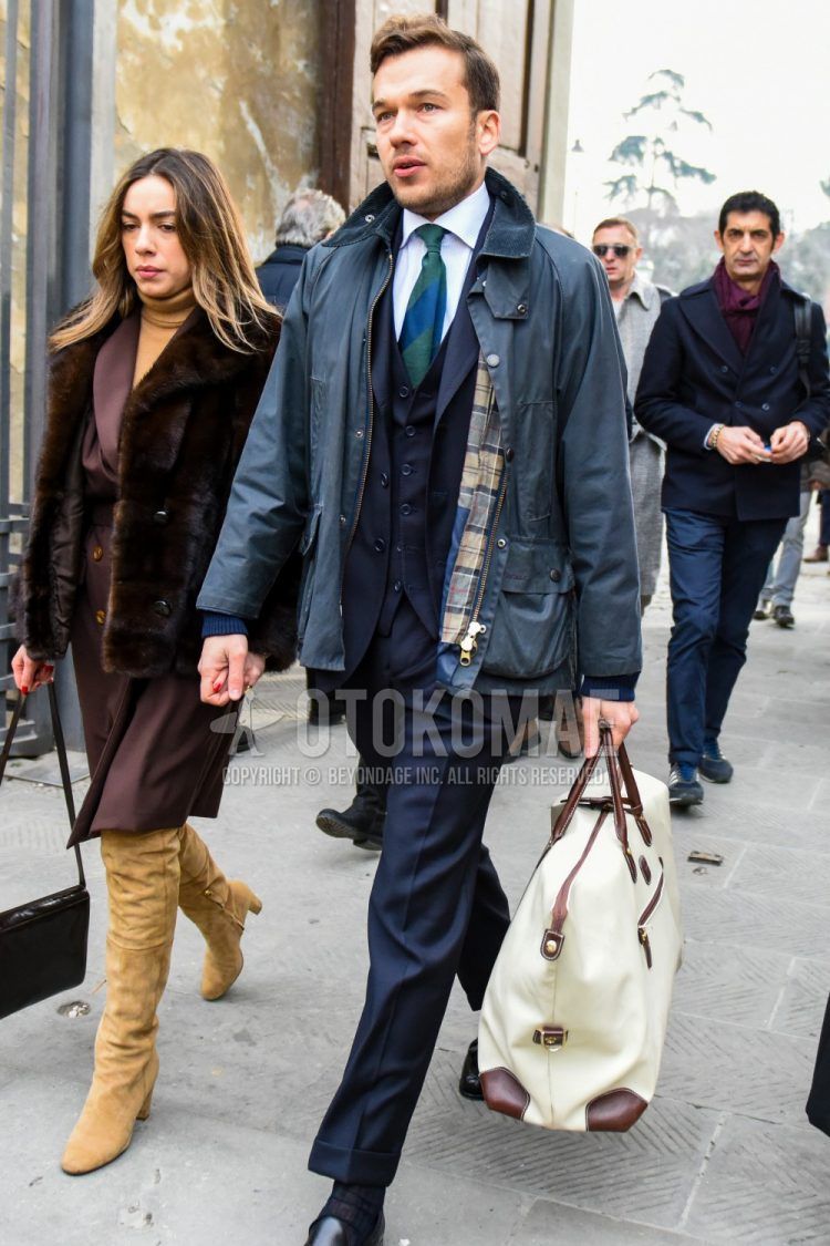 Men's coordinate and outfit with plain green field jacket/hunting jacket, plain white shirt, plain white Boston bag, plain navy three-piece suit, and plain green tie.