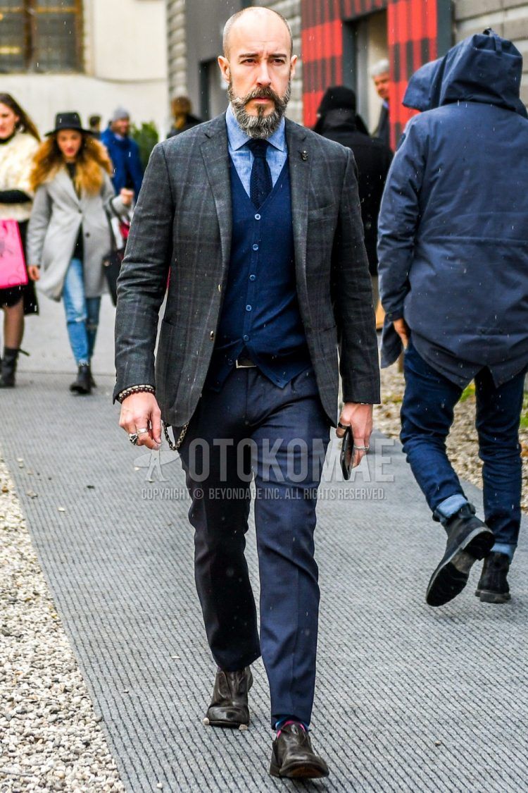 Men's coordinate and outfit with dark gray check tailored jacket, solid blue denim/chambray shirt, solid navy cardigan, solid dark gray slacks, multi-colored dotted socks, brown leather shoes, and solid navy knit tie.