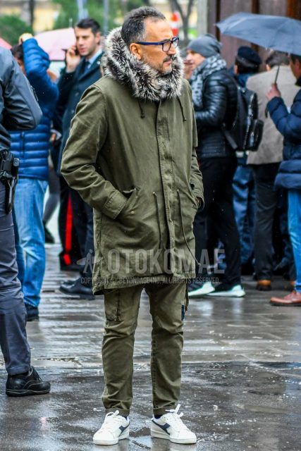 Men's coordinate and outfit with plain glasses, olive green plain mod coat, olive green plain cargo pants, and white low-cut sneakers by Diadora.