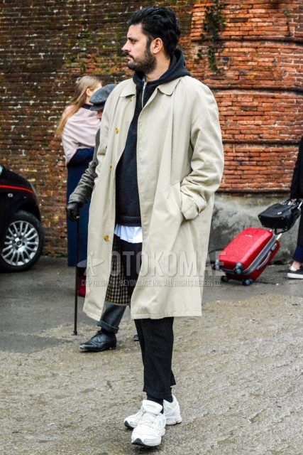 Winter men's coordinate and outfit with a solid beige stainless steel collar coat, solid black hoodie, solid white t-shirt, dark gray solid slacks, solid black socks, and Raf Simons Adidas Oswego white low-cut sneakers.