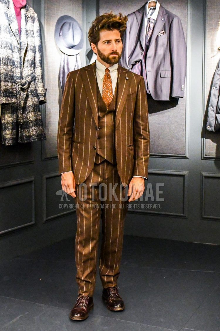 Men's coordinate and outfit with plain white shirt, brown plain toe leather shoes, brown striped three-piece suit, and graphic tie.