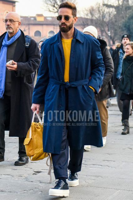 Men's coordinate and outfit with plain sunglasses, plain navy belted coat, plain yellow sweatshirt, plain navy cotton pants, plain navy socks, navy low-cut sneakers, and plain yellow Boston bag.