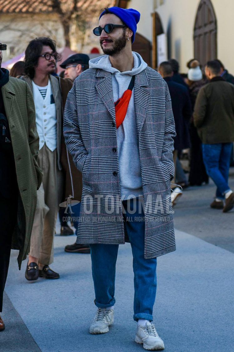 Winter men's coordinate/outfit with solid blue knit cap, solid black sunglasses, glen check gray checkered chester coat, solid gray hoodie, solid blue denim/jeans, solid white socks, white low-cut sneakers, and solid orange body bag.