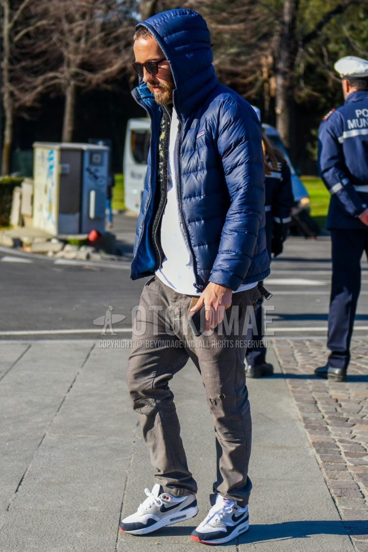 Men's coordinate and outfit with plain sunglasses, Patagonia plain blue down jacket, multi-colored top/underwear cardigan, plain white t-shirt, plain gray damaged jeans, Nike Air Max 1 white/gray low-cut sneakers.