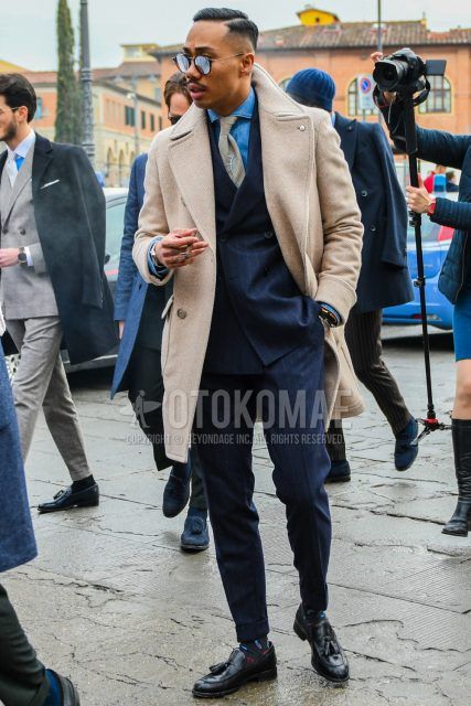 Winter men's coordinate and outfit with plain black sunglasses, plain beige Ulster coat, plain blue denim/chambray shirt, gray socks socks, black tassel loafer leather shoes, and navy striped suit.
