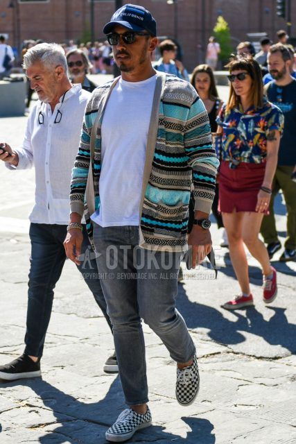 Men's coordinate and outfit with black graphic baseball cap, light blue/gray top/inner cardigan, plain white t-shirt, plain gray denim/jeans, and white/black low-cut sneakers by Vans.