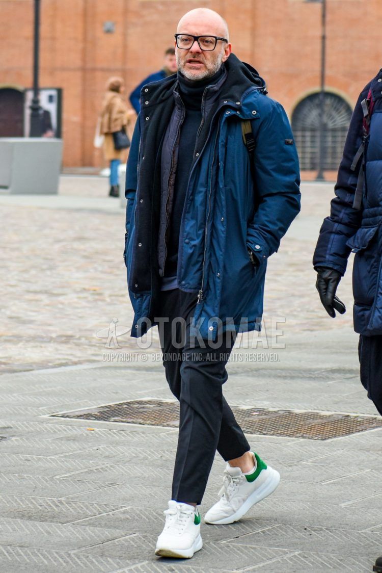 Men's winter coordinate and outfit with plain glasses, plain navy hooded coat, plain navy sweater, dark gray plain slacks, and Alexander McQueen white low-cut sneakers.