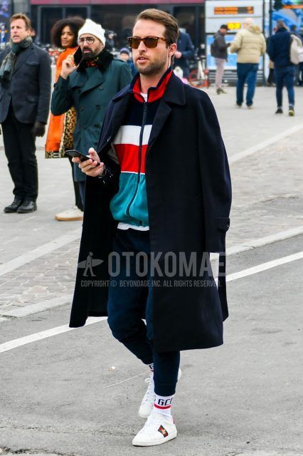 Brown tortoiseshell sunglasses, plain navy Ulster coat, plain white T-shirt, multi-colored striped sweatshirt, plain navy jogger pants/ribbed pants, plain navy sweatpants, Gucci white big logo socks, Gucci Ace white low-cut sneakers Men's coordinate and outfit.