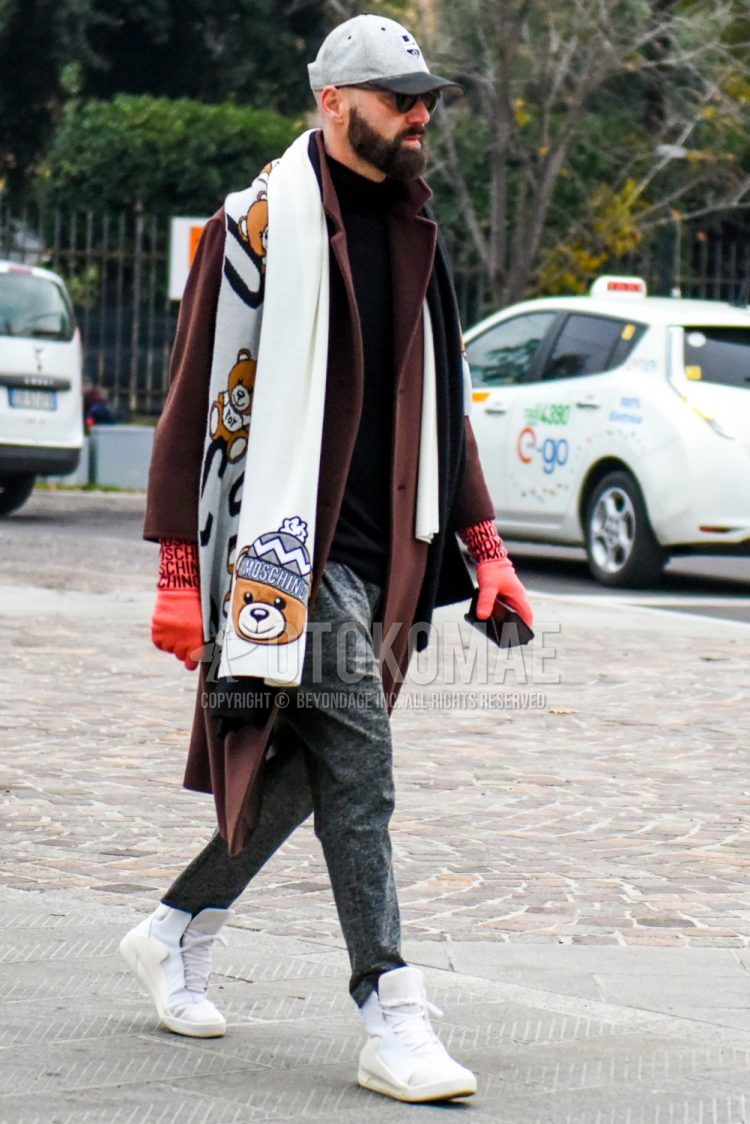 Men's winter/fall outfit with plain gray baseball cap, plain black sunglasses, Moschino white graphic scarf/stall, plain brown chester coat, plain black turtleneck knit, plain gray slacks, and white high-cut sneakers.