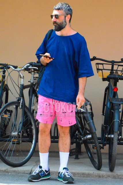Men's coordinate and outfit with solid beige sunglasses, solid navy t-shirt, pink bottom shorts, solid white socks, and New Balance 574 navy low-cut sneakers.