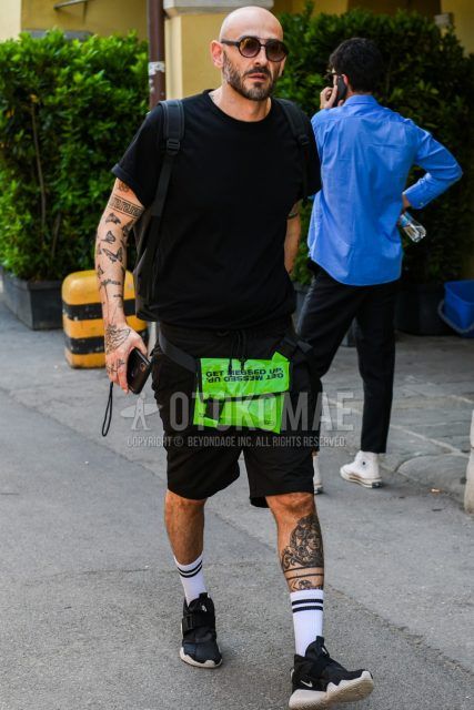 Men's coordinate and outfit with plain black/brown sunglasses, plain black t-shirt, plain black shorts, plain white socks, Nike black low-cut sneakers, and plain green body bag.