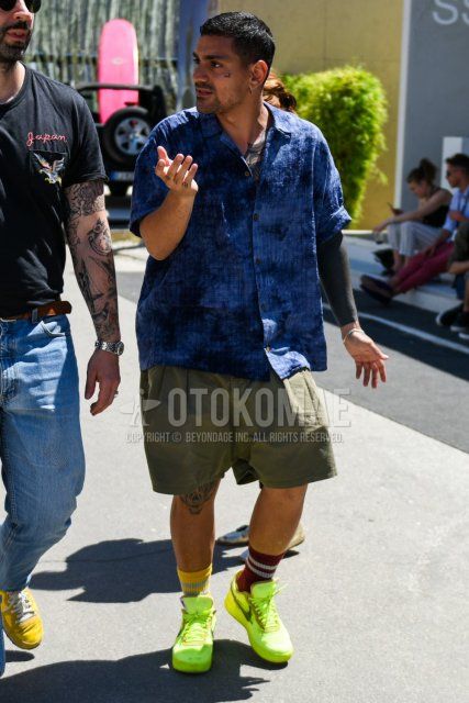 Men's coordinate and outfit with plain blue shirt, plain olive green shorts, red/yellow border socks, and Nike yellow-cut sneakers.