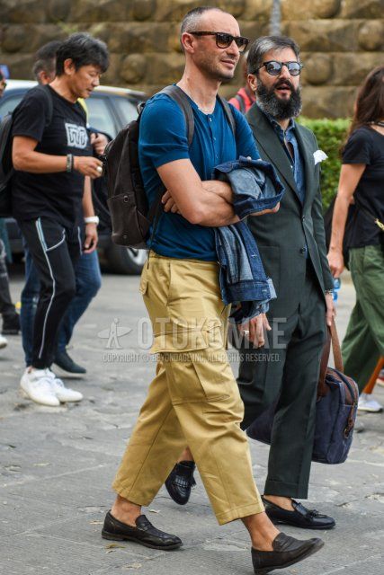 Men's coordinate and outfit with brown tortoiseshell sunglasses, plain blue t-shirt with henley neck, plain beige damaged jeans, plain cropped pants, plain cargo pants, black coin loafer leather shoes, and plain brown backpack.